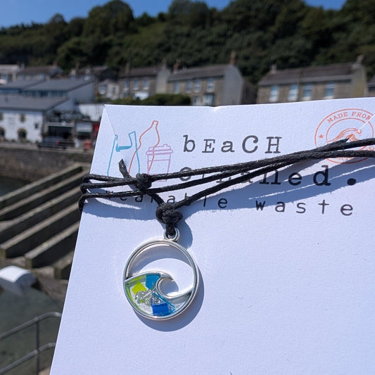 Sustainable ocean lover wave necklace gift. Wave shaped siver necklace with beach plastic pollution set within it on a black adjustable cord made from seaweed and cotton.