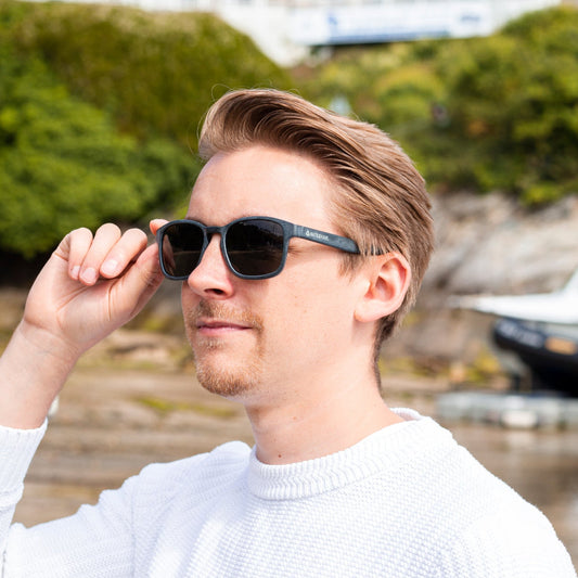 Man wearing grey recycled ocean plastic sunglasses with a blurred natural background