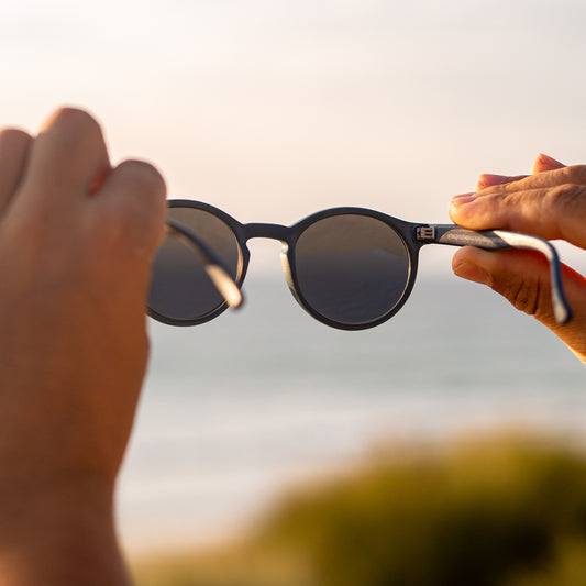 navy recycled plastic sunglasses view from behind as they're held up to the sunset.
