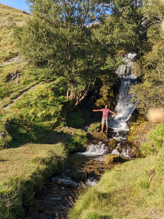 Man finding serenity by a captivating waterfall, wearing 'Into the wilderness I go to lose my mind and find my soul' t-shirt by Arvor Life