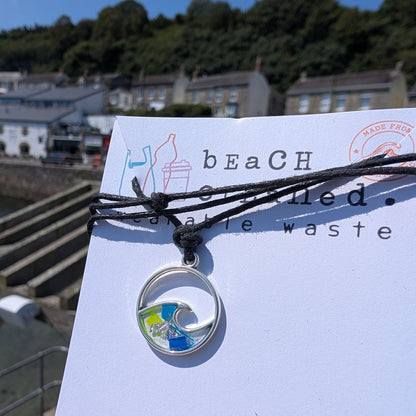 Sustainable ocean lover wave necklace gift. Wave shaped siver necklace with beach plastic pollution set within it on a black adjustable cord made from seaweed and cotton. 