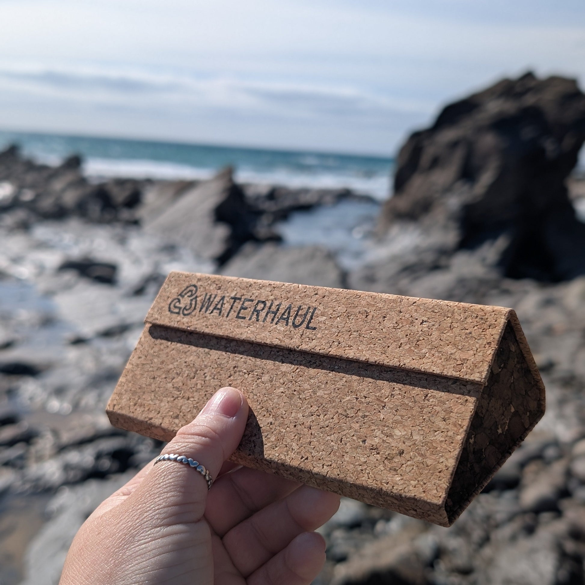 Eco-friendly cork sunglasses case held by a hand with a beach background
