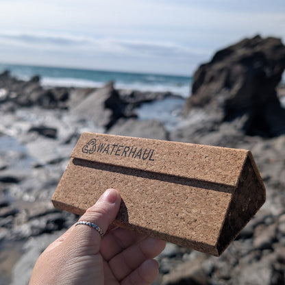 Eco-friendly cork sunglasses case held by a hand with a beach background