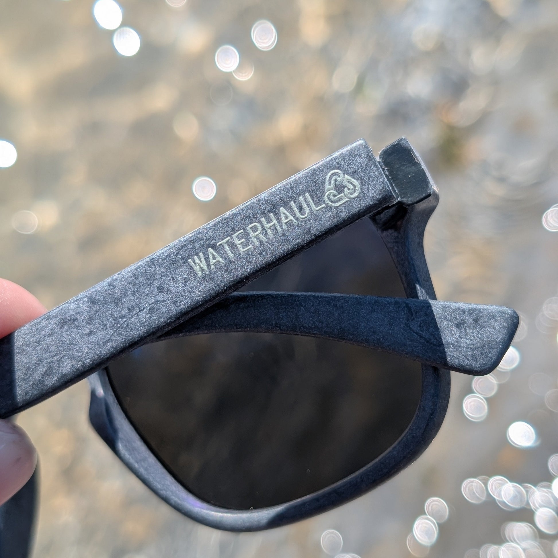 waterhaul logo on the slate grey sunglasses held by the sea
