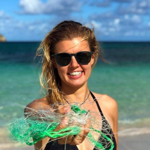 Lady wearing grey recycled plastic sunglasses on a beach holding ghost nets