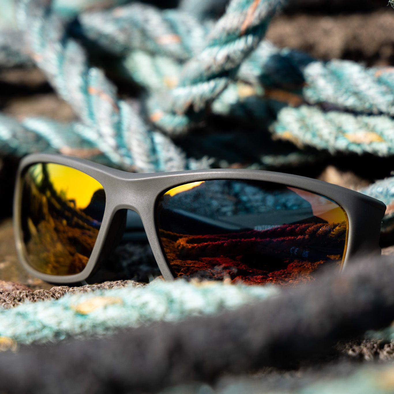 Wrap-around eco-friendly sunglasses with reflective orange mirrored lenses, made from recycled fishing nets recovered from UK beaches. 