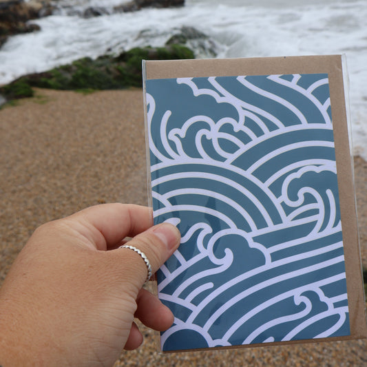 Hand holding an ocean waves card with wave pattern against a beach background