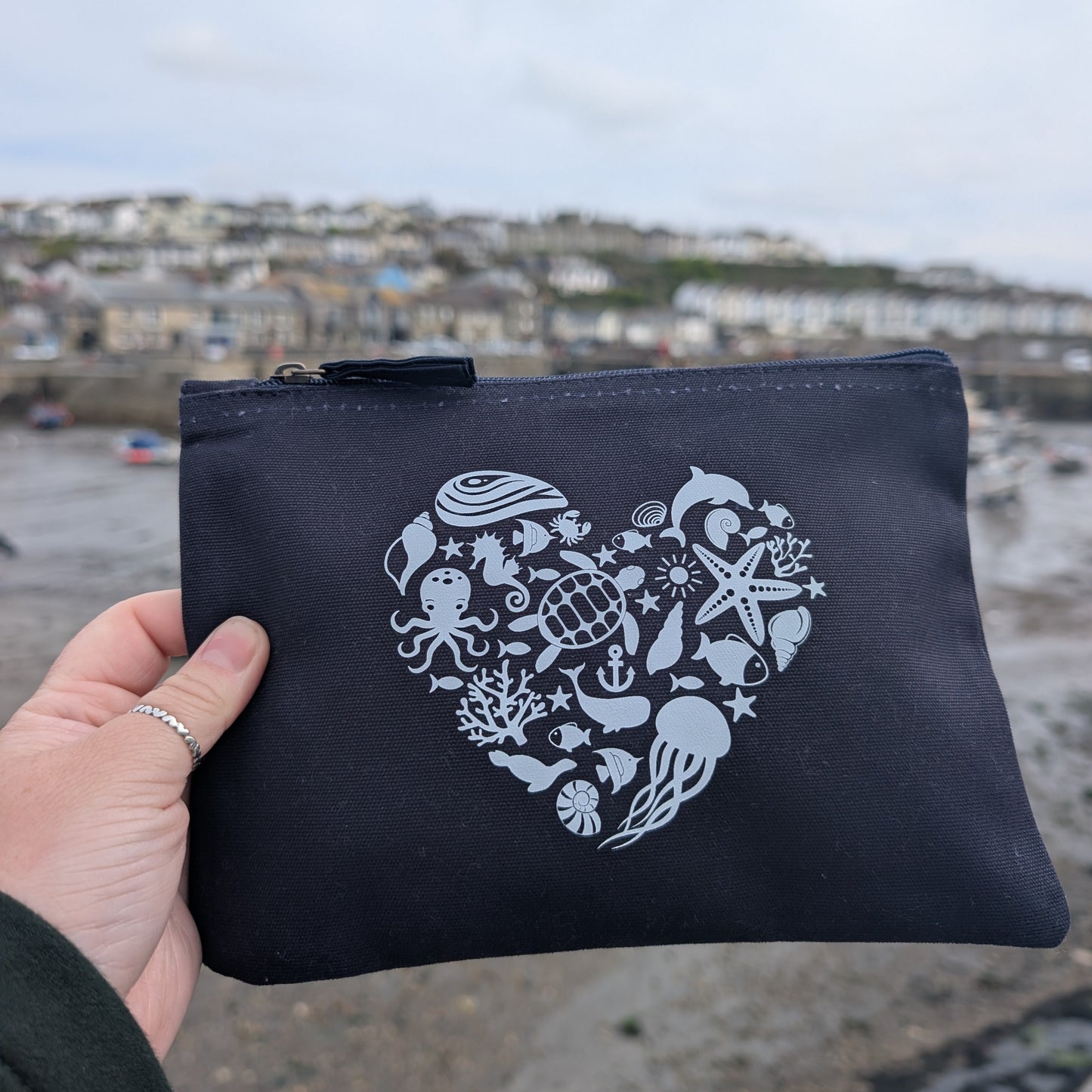 Navy pouch with white sea-themed design held by a hand, with a coastal background.