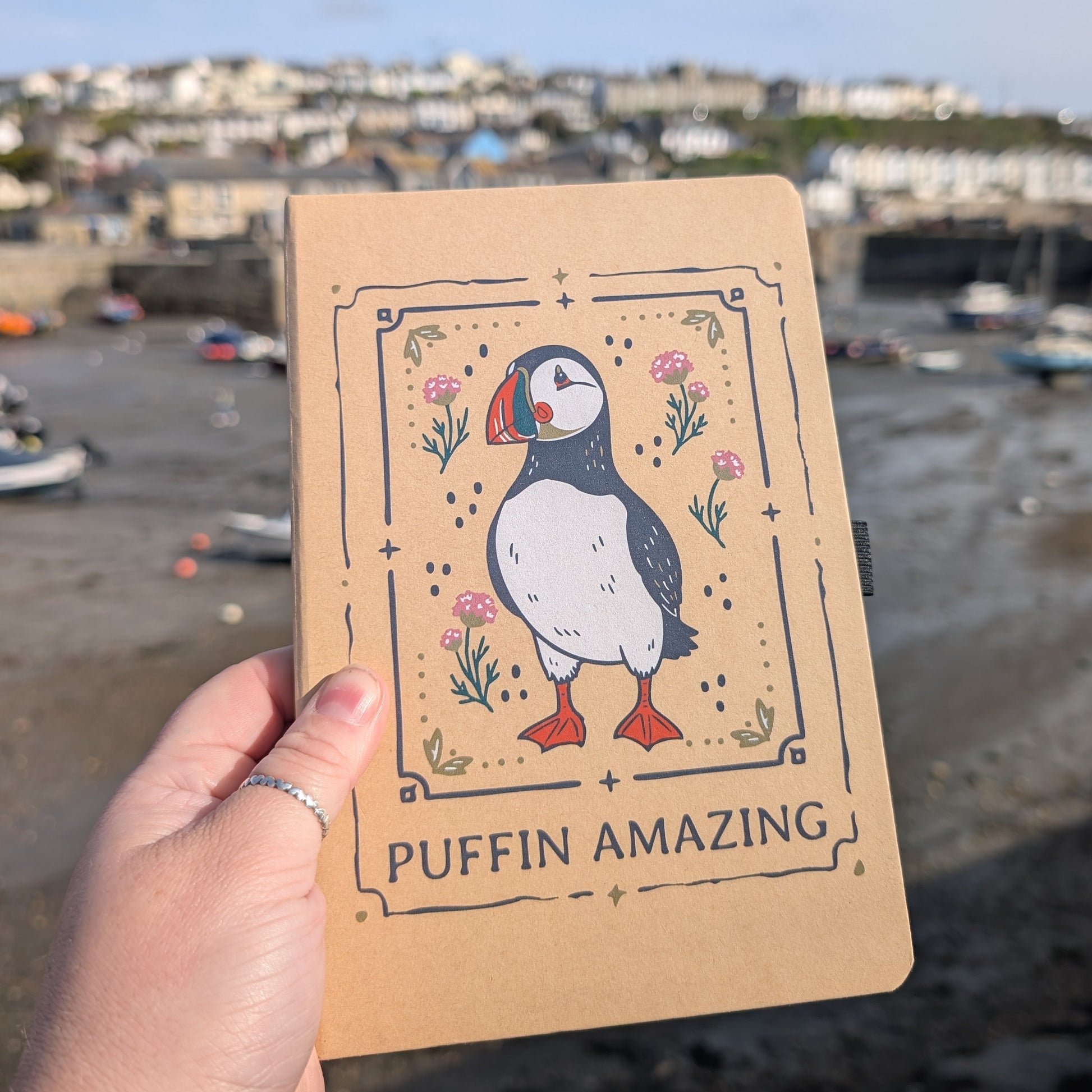 Notebook with puffin illustration held in front of a coastal scene