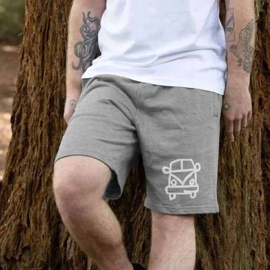 Person wearing gray shorts with a white campervan graphic design, standing against a tree.