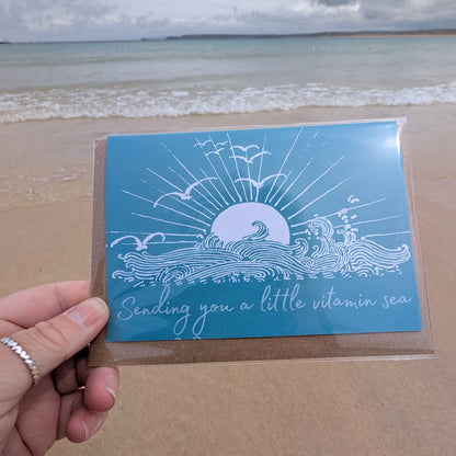 Sending A Little Vitamin Sea Greeting Card with ocean design held by a hand on a beach
