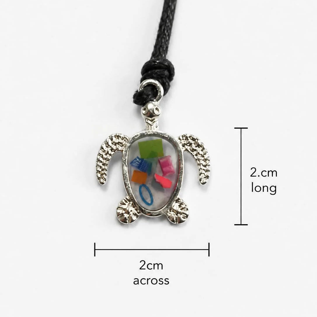 A sea turtle pendant necklace with a silver-plated turtle and beach plastic set in a bioresin, shown on a black seaweed and cotton cord against a light gray background with measurement labels indicating 2 cm length and 2 cm width.