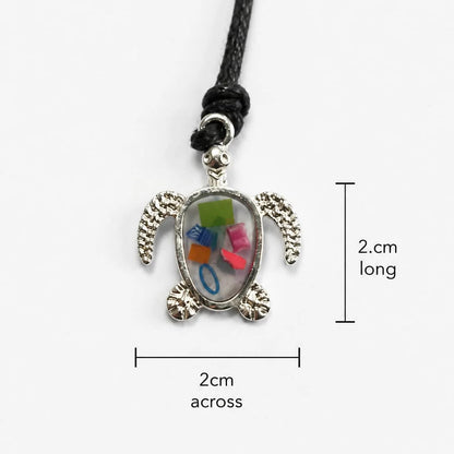 A sea turtle pendant necklace with a silver-plated turtle and beach plastic set in a bioresin, shown on a black seaweed and cotton cord against a light gray background with measurement labels indicating 2 cm length and 2 cm width.