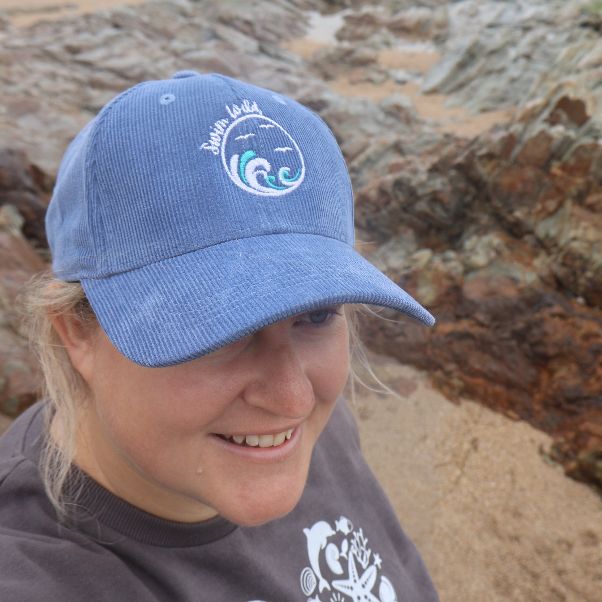 Person wearing a blue organic cotton swim wild hat on a rocky beach