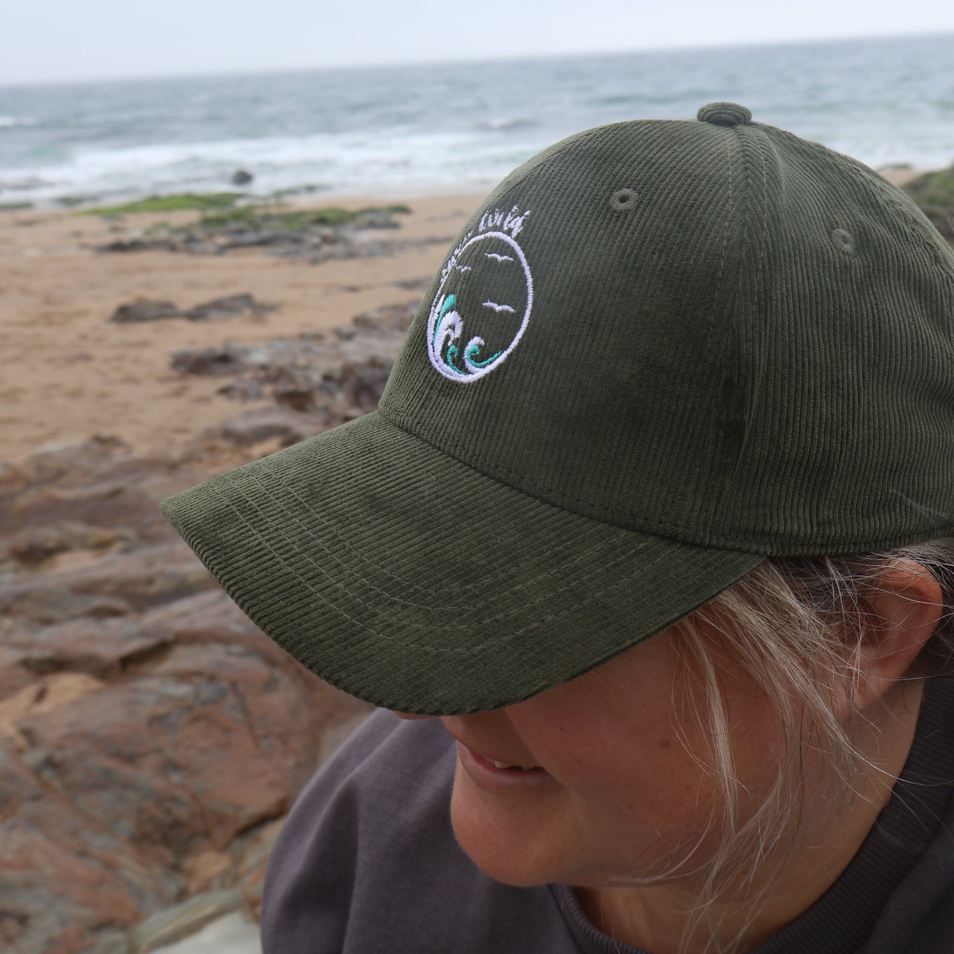 Person wearing a green wild swimming cap with a logo, standing on the beach.
