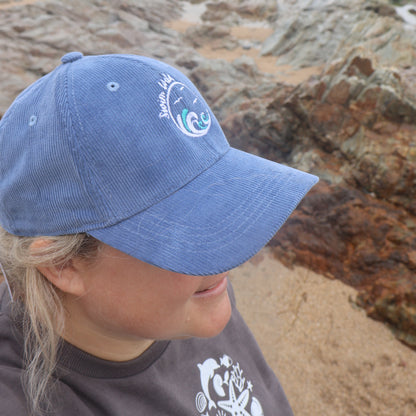 Person wearing a blue wild swimming hat, standing on a rocky beach.