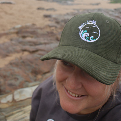 Person wearing a green cap with a wild swimming logo on a beach