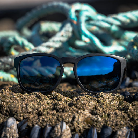 Recycled ocean plastic sunglasses on a rock with ropes and water in the background