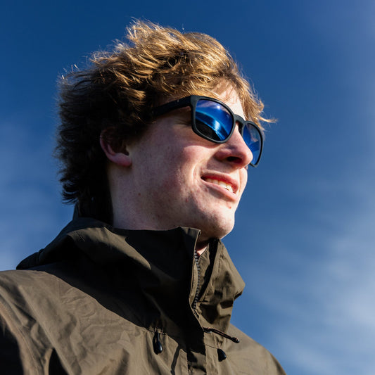 Person wearing black sunglasses with a blue mirror polarised lens against a blue sky.