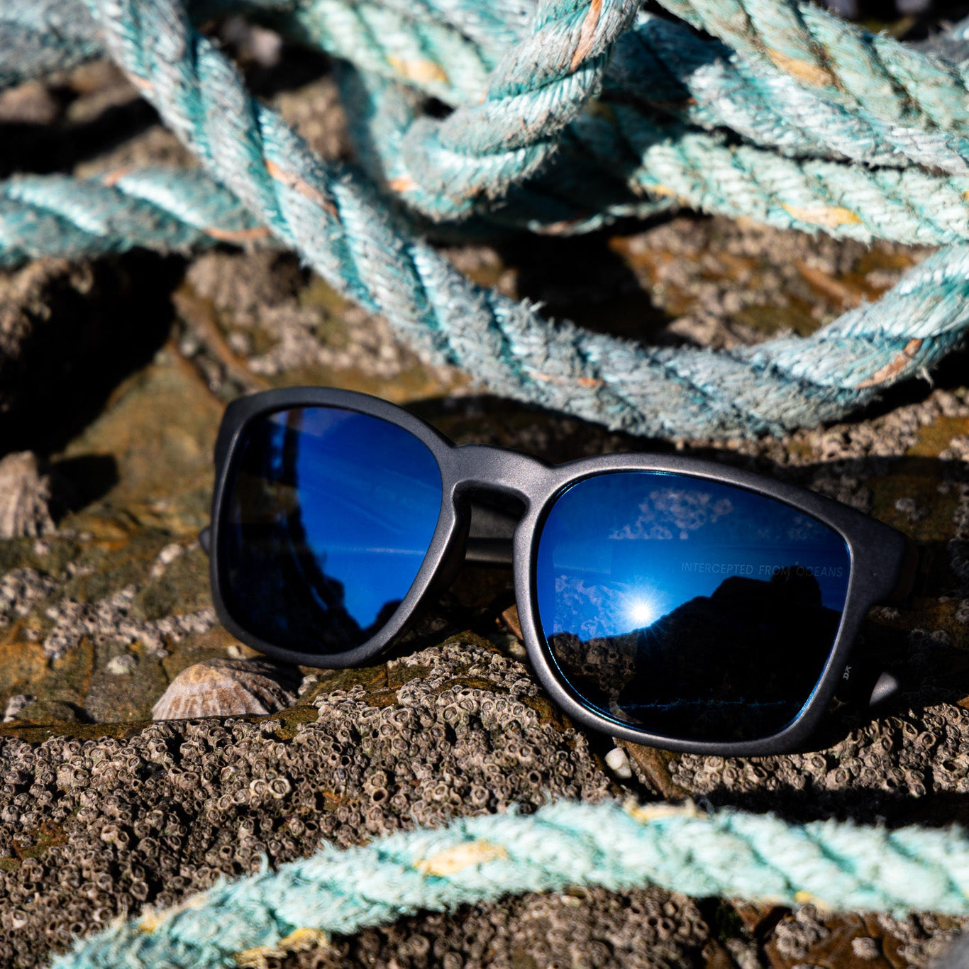 Waterhaul recycled sunglasses with blue reflective lens on a textured surface with ropes