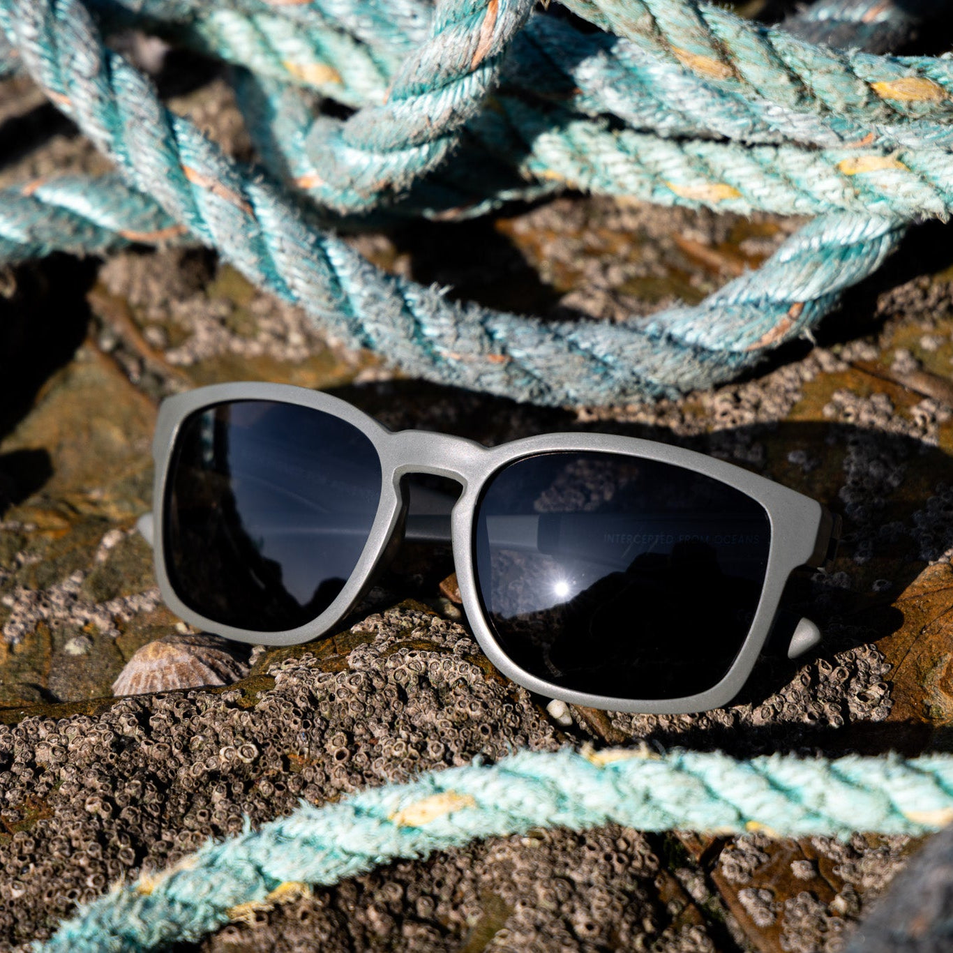 Sunglasses made from recycled nets on a textured surface with ghost fishing gear in the background