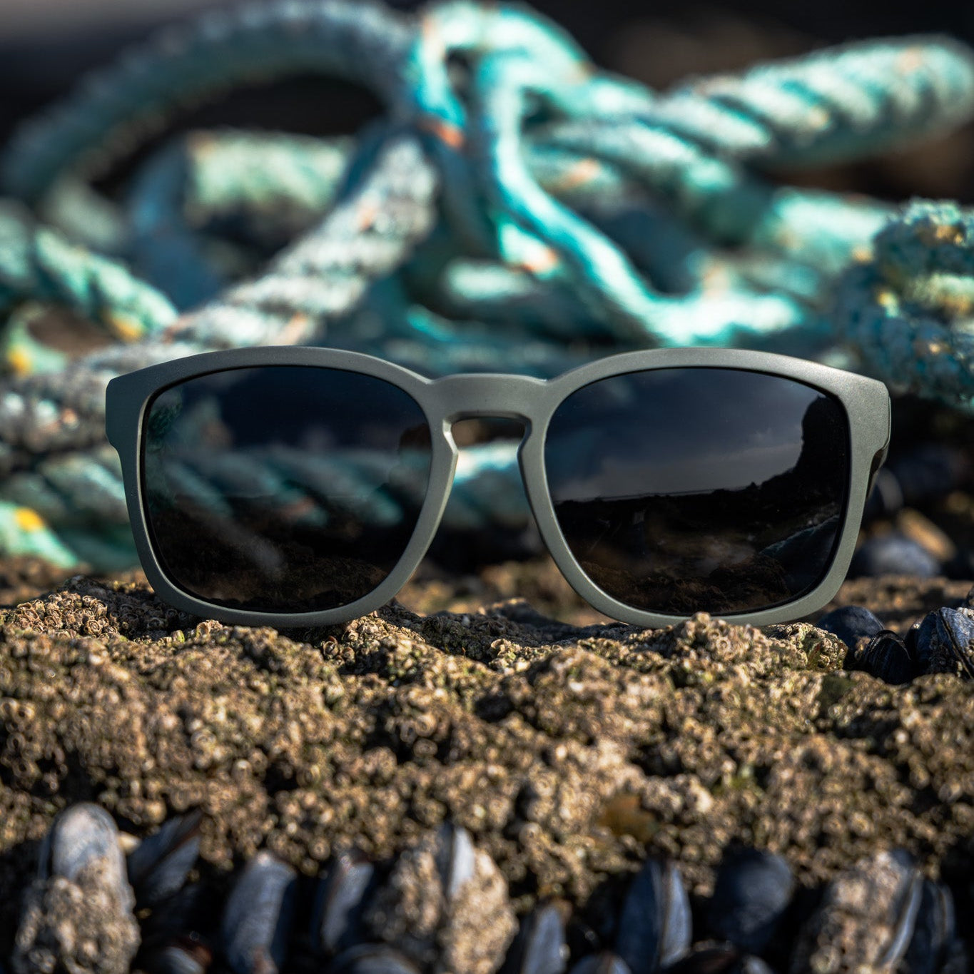 Recycled plastic polarised sunglasses on a sandy surface with ropes in the background