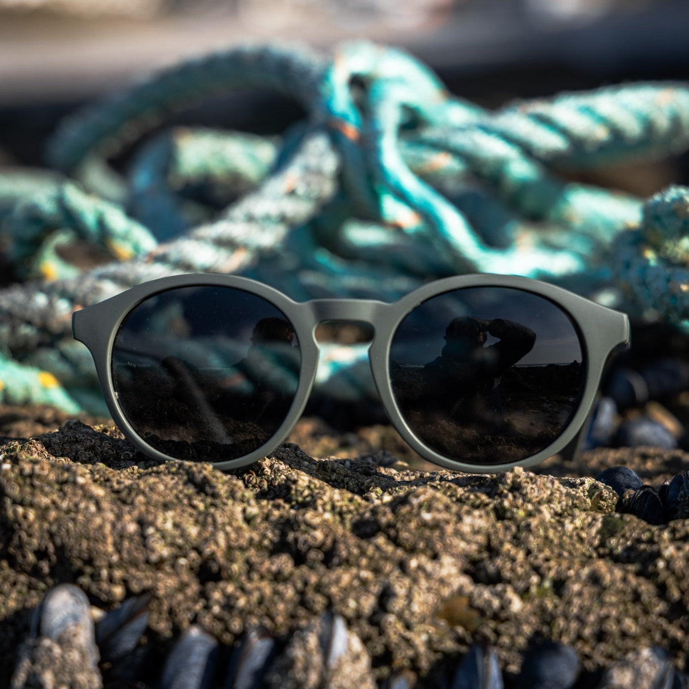 Recycled ghost net sunglasses on a sandy surface with ropes in the background