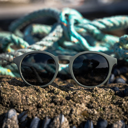 Recycled ghost net sunglasses on a sandy surface with ropes in the background