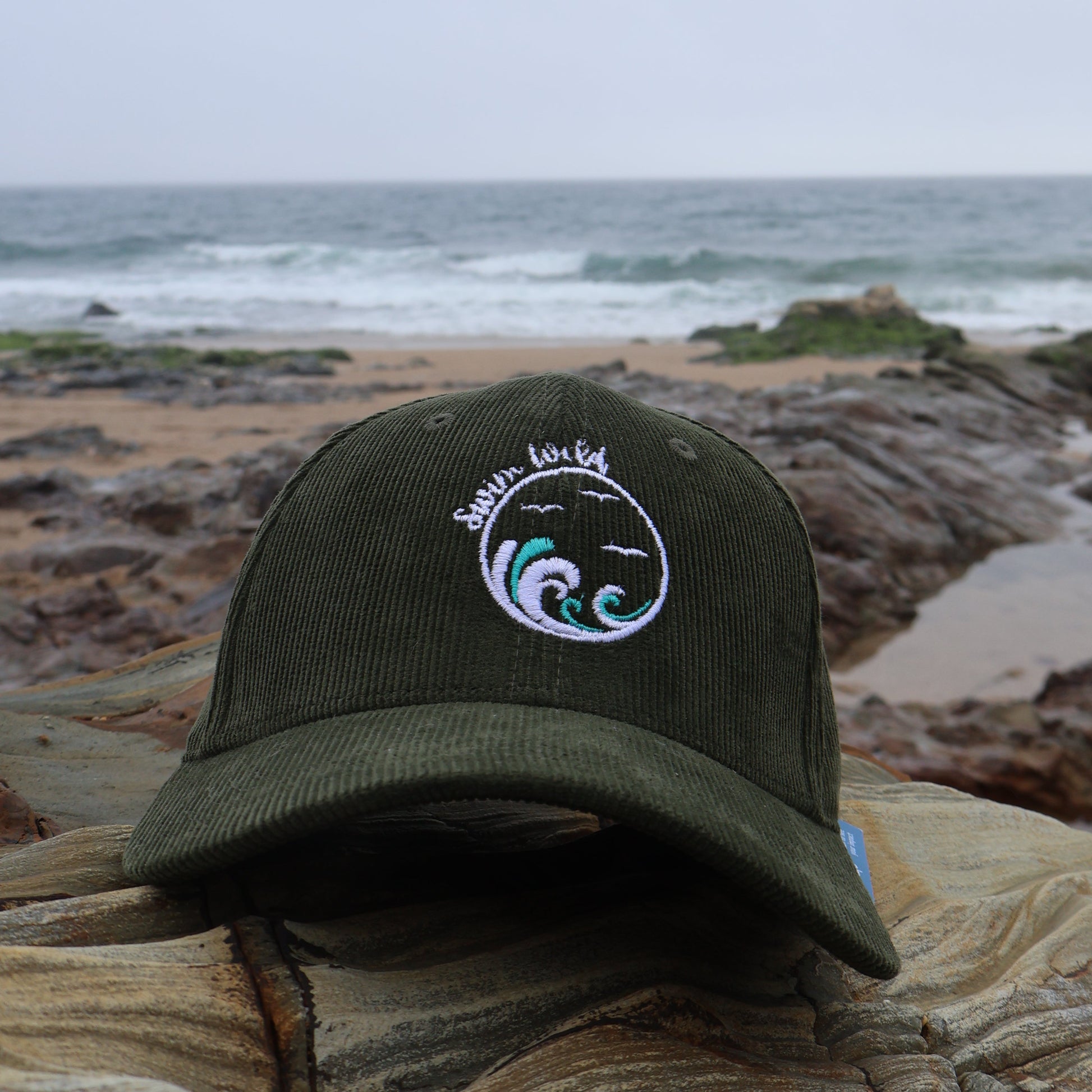 Green organic cotton hat with a wild swimming design on a rock by the ocean