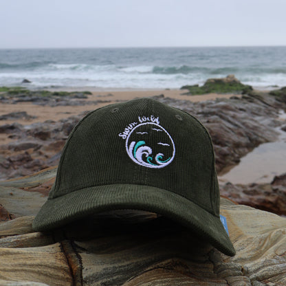Green organic cotton hat with a wild swimming design on a rock by the ocean
