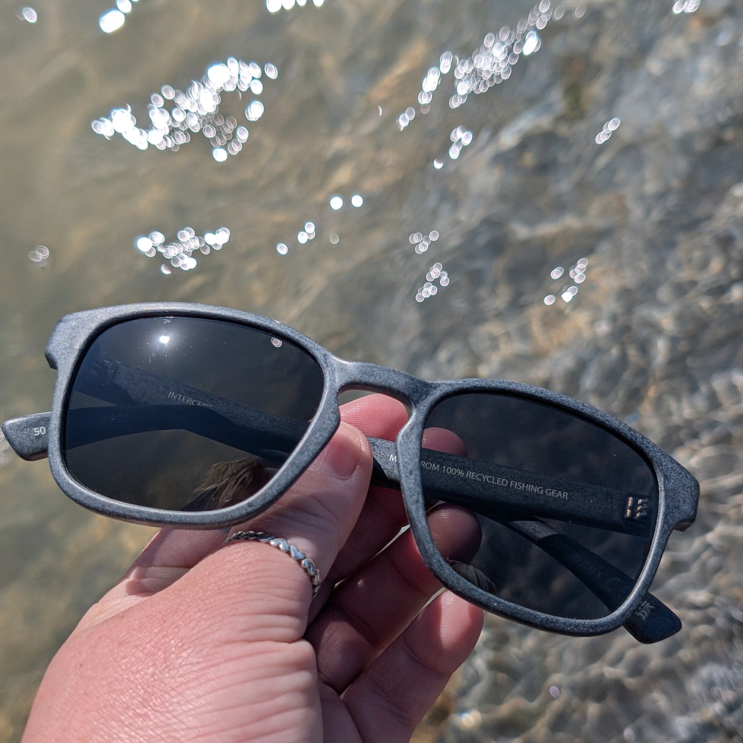 Grey sunglasses made from recycled ocean plastic on a beach