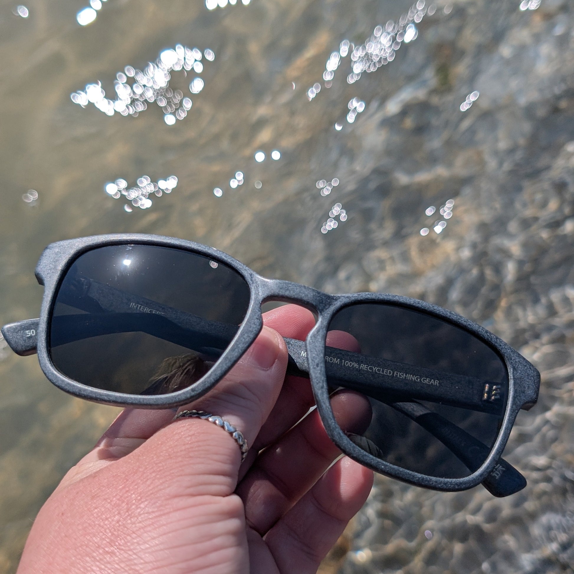 Grey sunglasses made from recycled ocean plastic on a beach