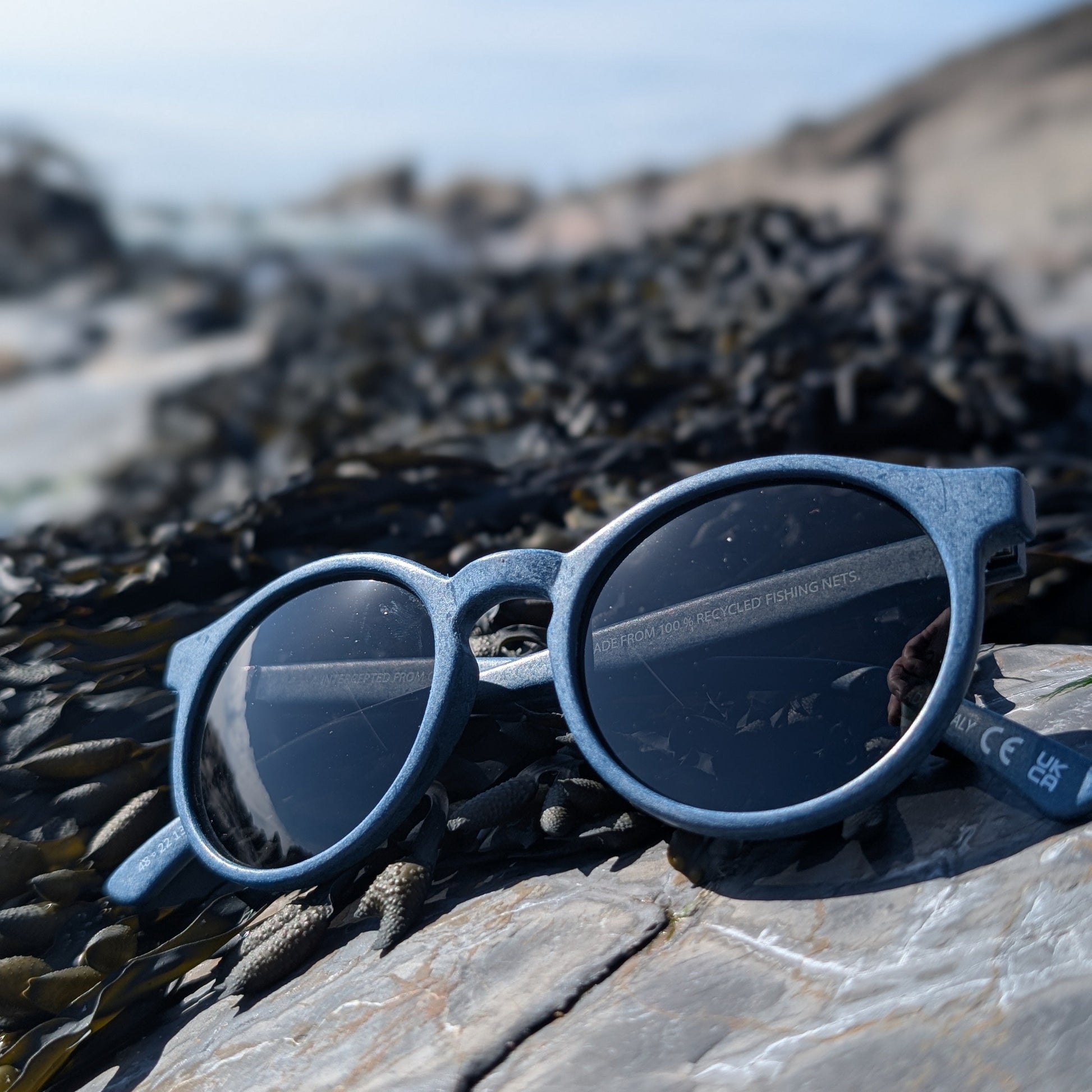 Navy rounded sunglasses made with recycled fishing nets on the beach 