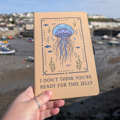 Notebook with jellyfish illustration and text held by a hand against a coastal background