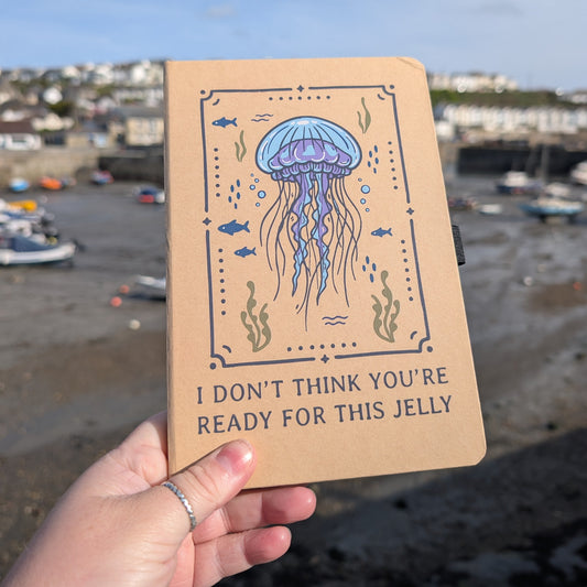 Notebook with jellyfish illustration and text held by a hand against a coastal background