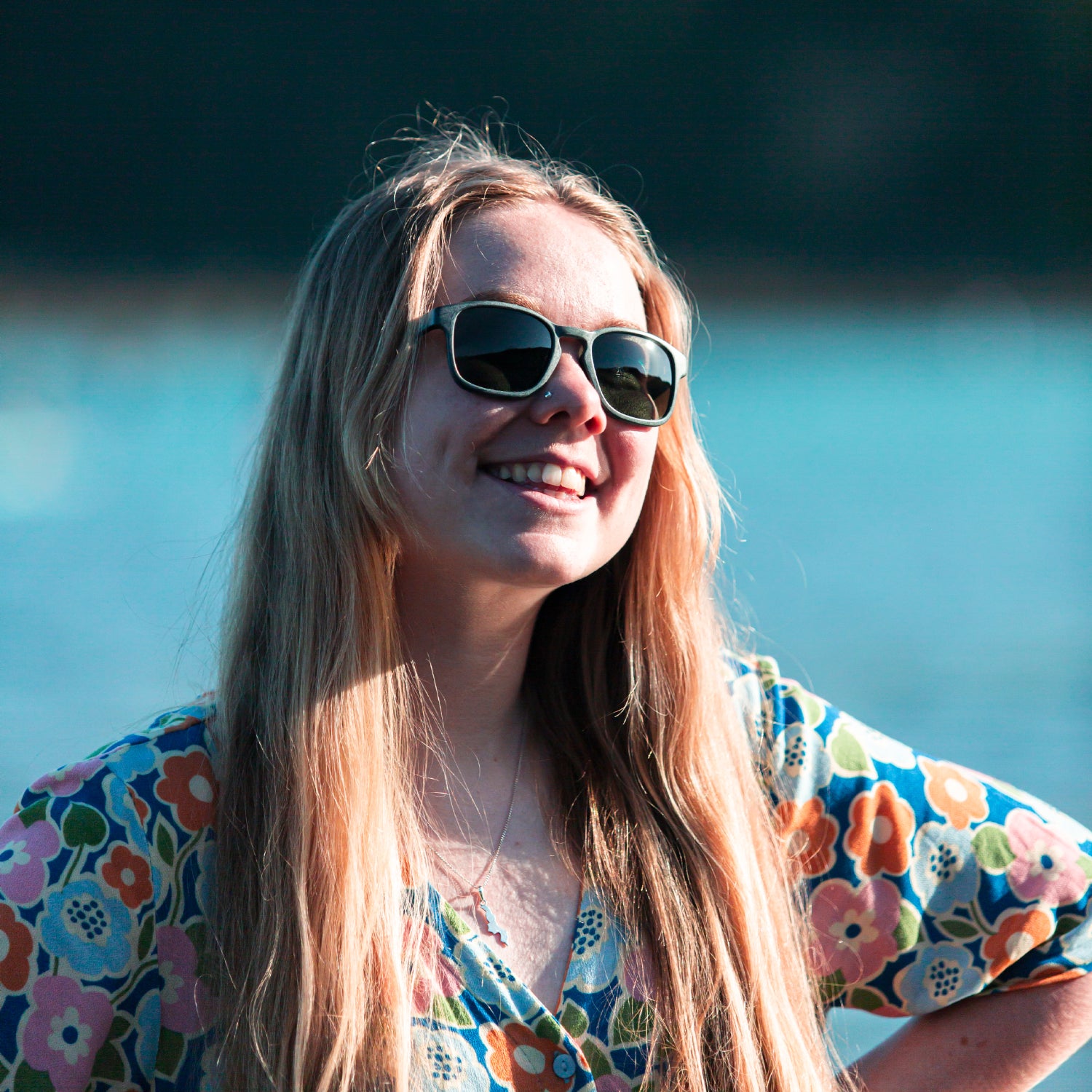 Woman wearing waterhaul recycled plastic sunglasses and a floral dress with a blurred background