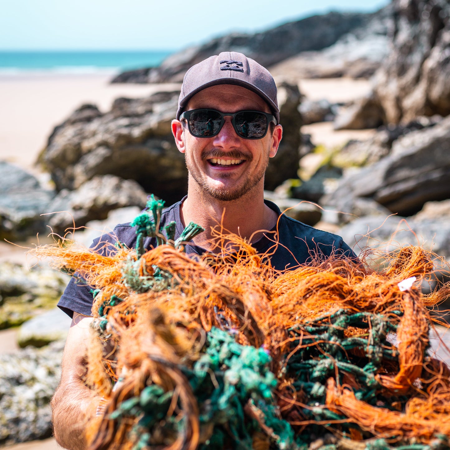 Man wearing sunglasses made from recycled ghost nets holding ghost nets on the beach