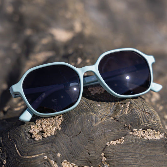 Recycled beach plastic Sunglasses with light blue frames and dark lenses on a textured surface
