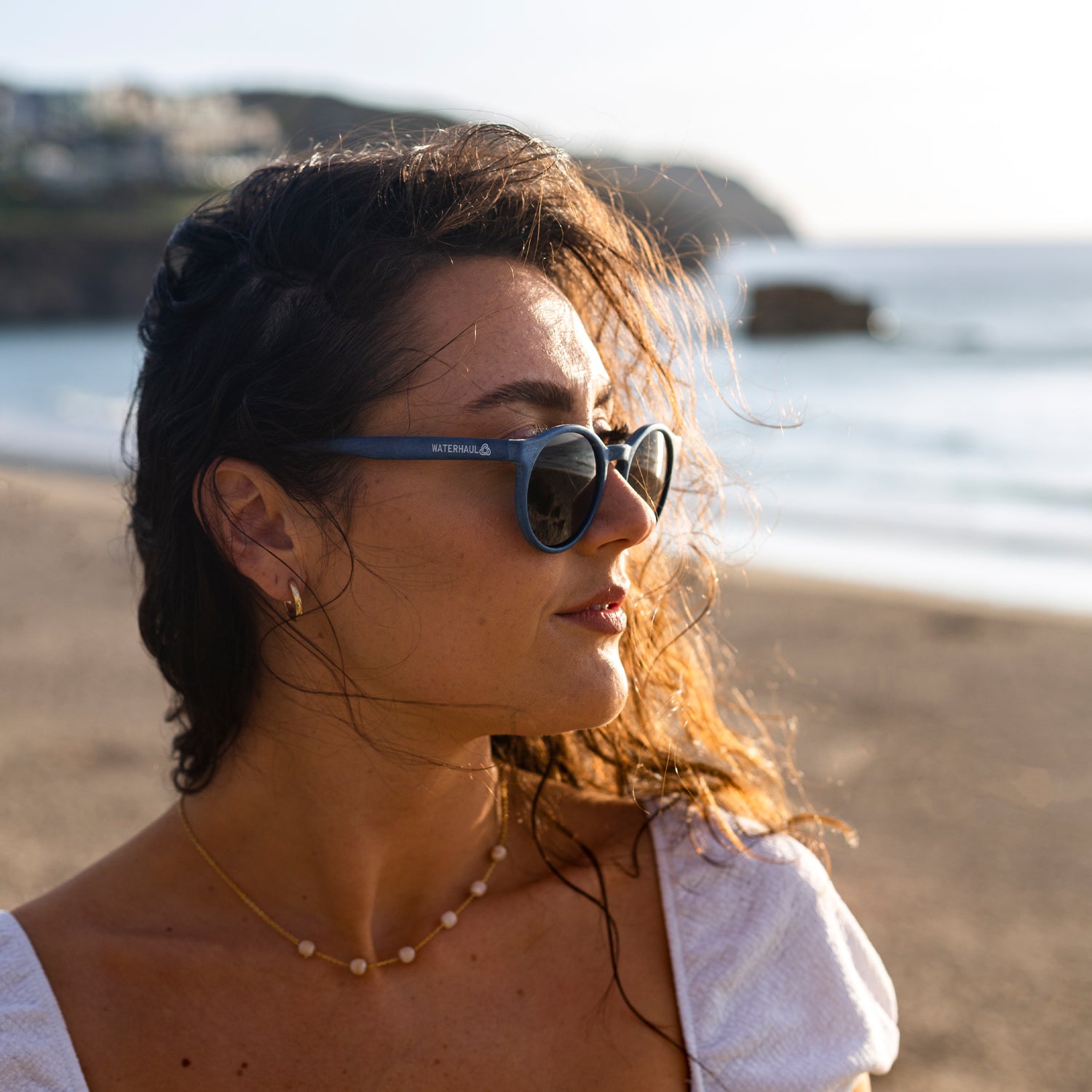 Lady wearing navy recycled sunglasses with a rounded frame on the beach