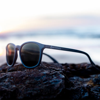navy waterhaul sunglasses sitting on a rock as sunset showing side view with logo 
