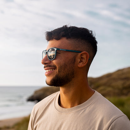 Man wearing navy sunglasses made with recycled plastic with a scenic background of water and rocks