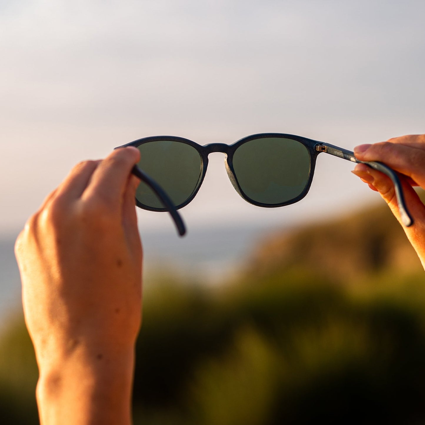 Person holding navy recycled plastic sunglasses with a blurred natural background
