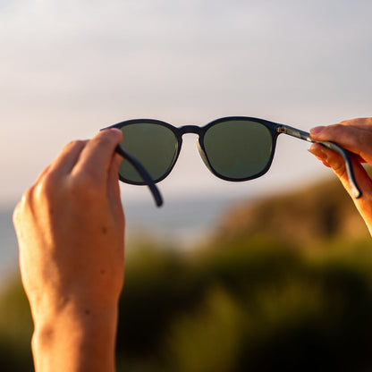 Person holding navy recycled plastic sunglasses with a blurred natural background