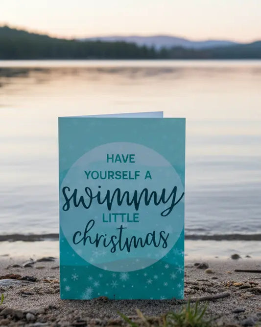 A Christmas greeting card with a swimming-themed message 'Have yourself a swimmy little Christmas' sitting next to a wild swimming lake.